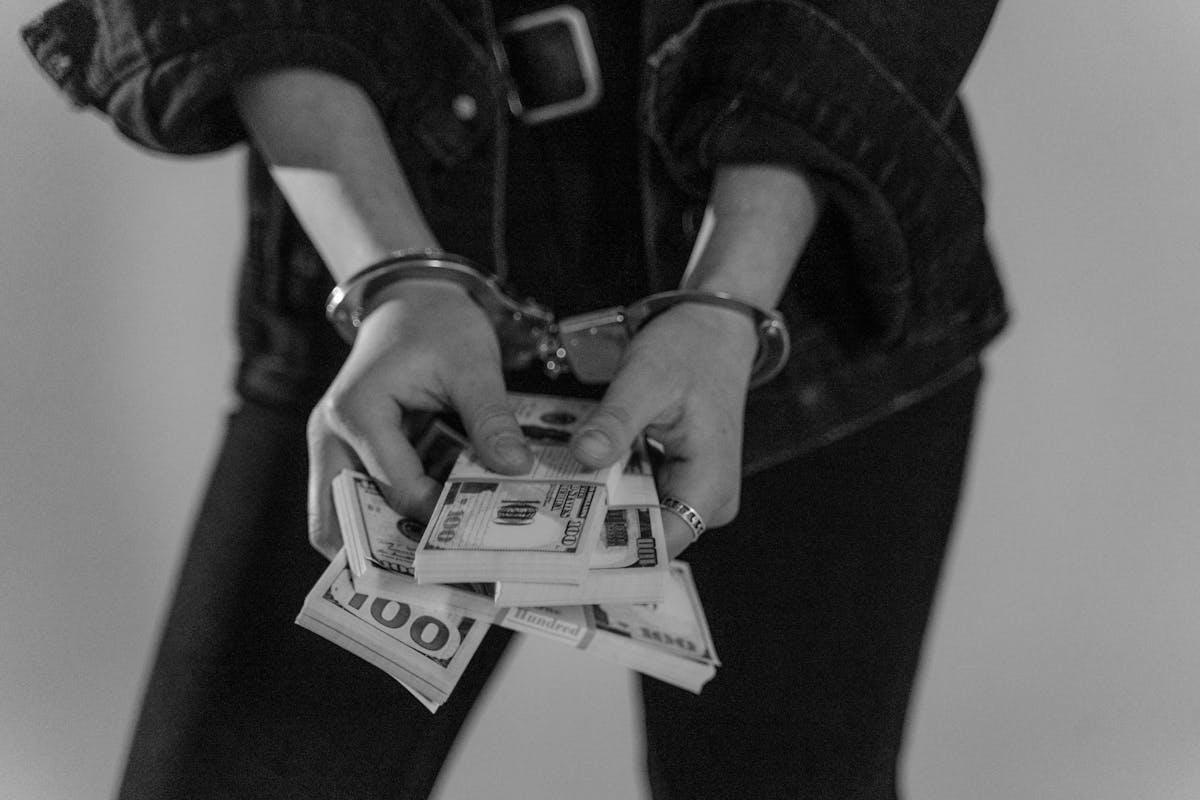 Black and white image of a handcuffed person holding bundles