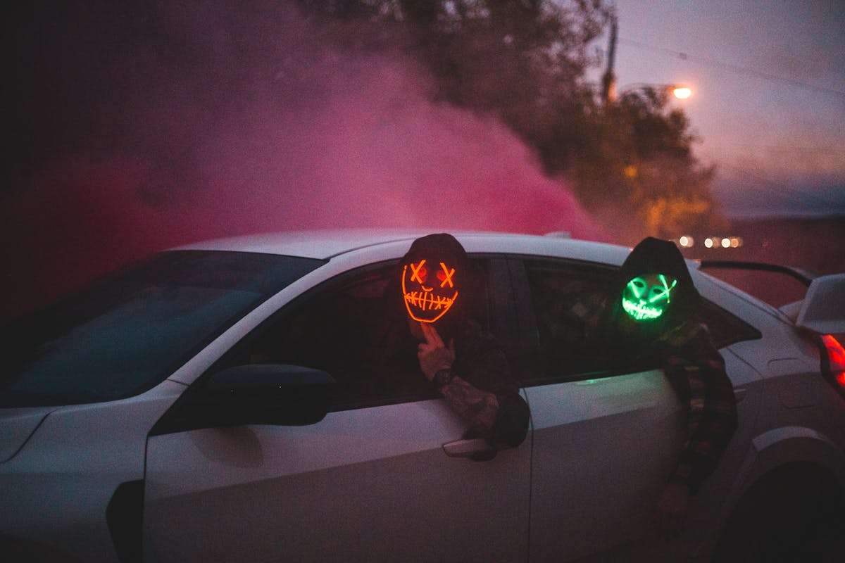 Unrecognizable men in glowing Halloween masks driving car